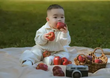 Cute baby playing with apples on a picnic mat outdoors in daylight.