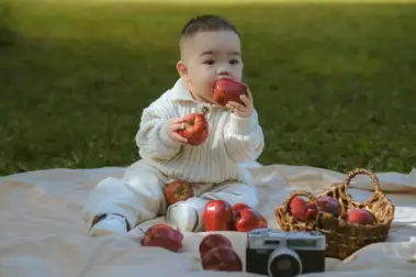 Alimentação saudável na educação infantil: segredos revelados! Cute baby playing with apples on a picnic mat outdoors in daylight.