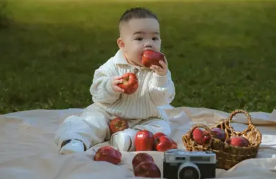 Cute baby playing with apples on a picnic mat outdoors in daylight.