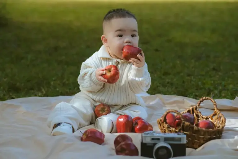 Alimentação saudável na educação infantil: segredos revelados! Cute baby playing with apples on a picnic mat outdoors in daylight.