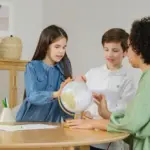 Children and teacher exploring globe for geography lesson indoors.
