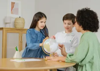 Children and teacher exploring globe for geography lesson indoors.