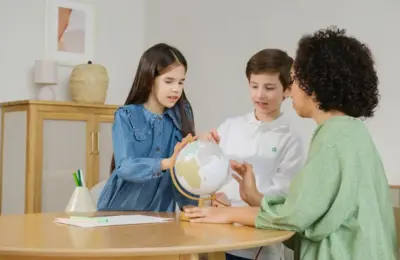 Children and teacher exploring globe for geography lesson indoors.