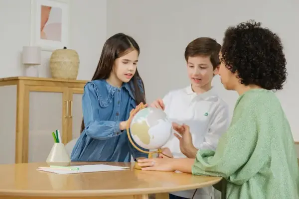 Children and teacher exploring globe for geography lesson indoors.