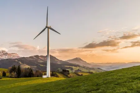 Tecnologia Sustentável: Descubra Inovações que Transformam o Futuro Wind turbine amid rolling hills and mountains at sunset, symbolizing renewable energy and sustainability.