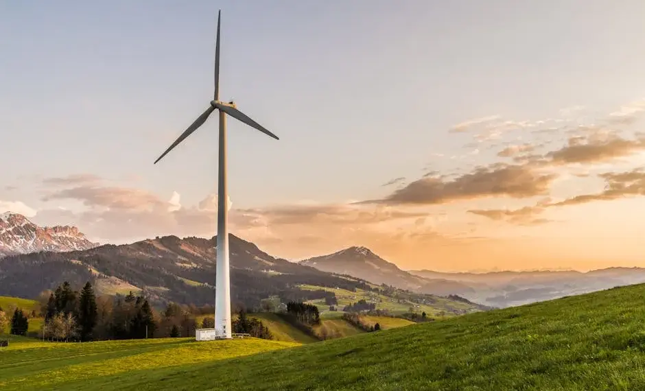 Wind turbine amid rolling hills and mountains at sunset, symbolizing renewable energy and sustainability.