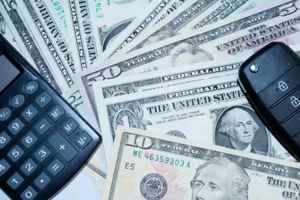 US dollars, calculator, and car keys representing finance and investment tools.