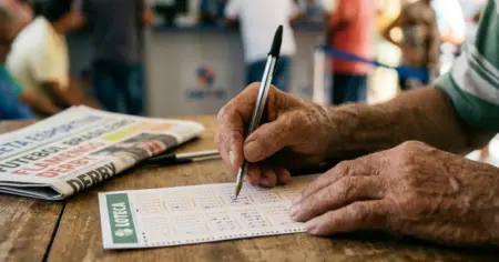 Close-up ultra-realista das mãos de um homem idoso preenchendo com entusiasmo um volante da Loteca com uma caneta em uma mesa de madeira dentro de uma lotérica movimentada e ensolarada no Brasil.